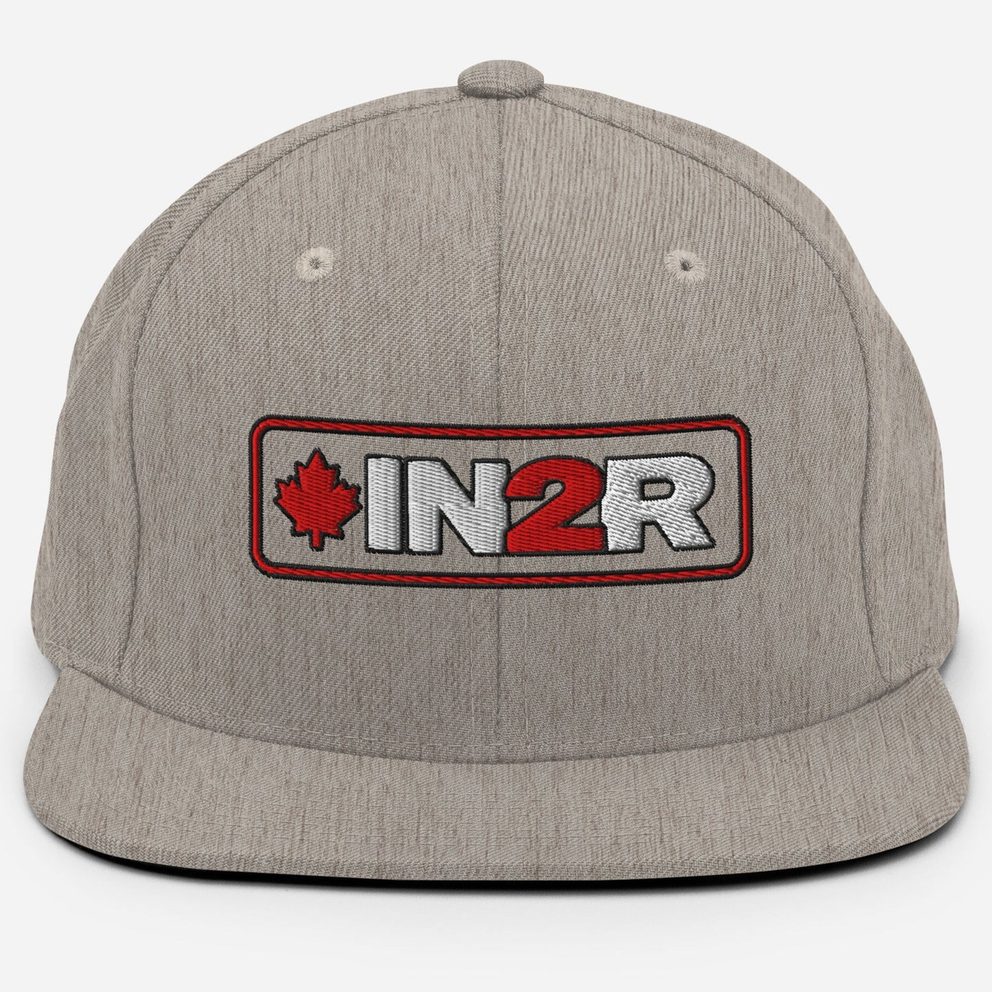 A heather gray snapback cap featuring a rectangular embroidered patch on the front with a red maple leaf, the text 'IN2R' in white and red, and a red border.