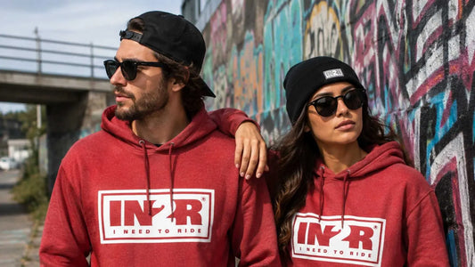 Two people wearing red IN2R Original hoodies beside a colourful graffiti wall.