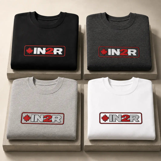 Four folded crewneck sweatshirts arranged in a 2x2 grid on light beige display blocks. The top-left is black, the top-right is dark gray, the bottom-left is light gray, and the bottom-right is white.