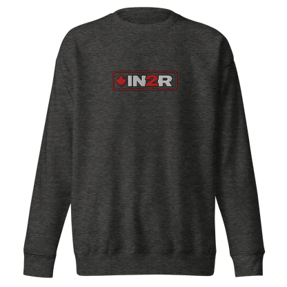A dark heather gray crewneck sweatshirt featuring a rectangular chest graphic with the text 'IN2R' in white and red, flanked by a red maple leaf icon, set against a plain white background.