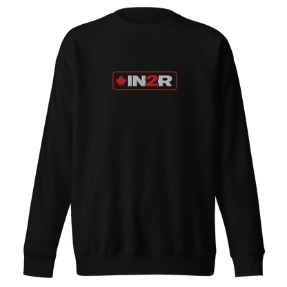 A black crewneck sweatshirt with a rectangular chest graphic that reads 'IN2R' in white and red, featuring a small red maple leaf on the left side, shown against a plain white background.