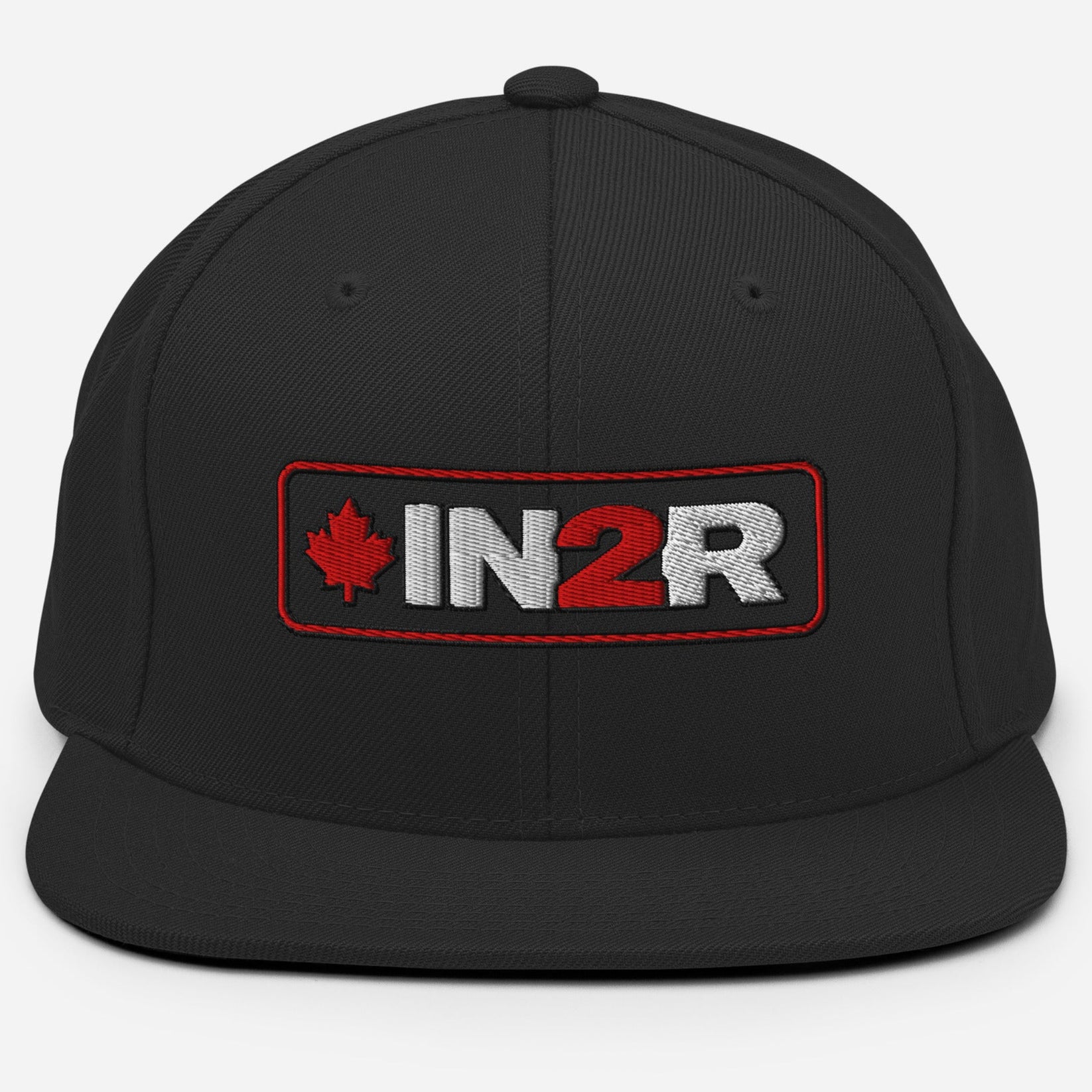 A black snapback cap featuring a rectangular embroidered patch on the front with a red maple leaf, the text 'IN2R' in white and red, and a red border.