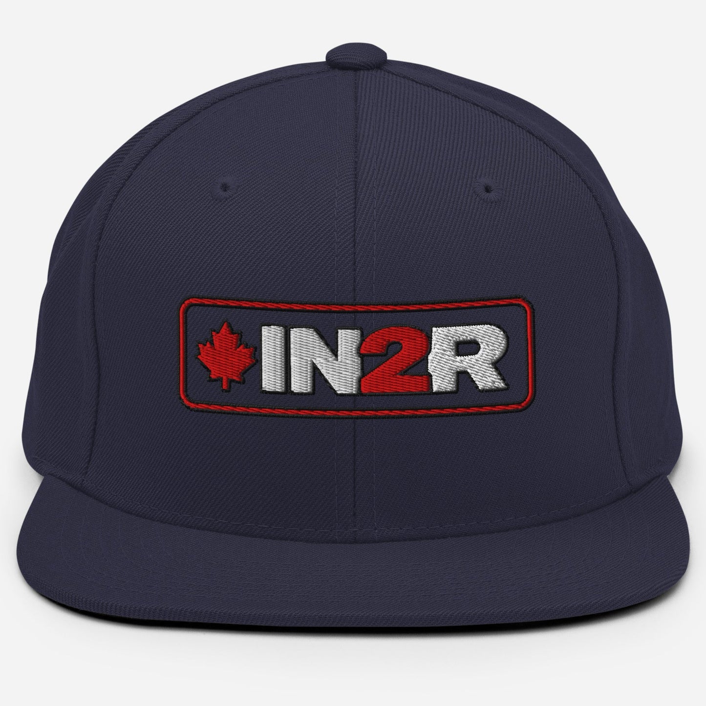 A navy blue flat-brim cap featuring a rectangular embroidered patch on the front with a red maple leaf, the text 'IN2R' in white and red, and a red border.