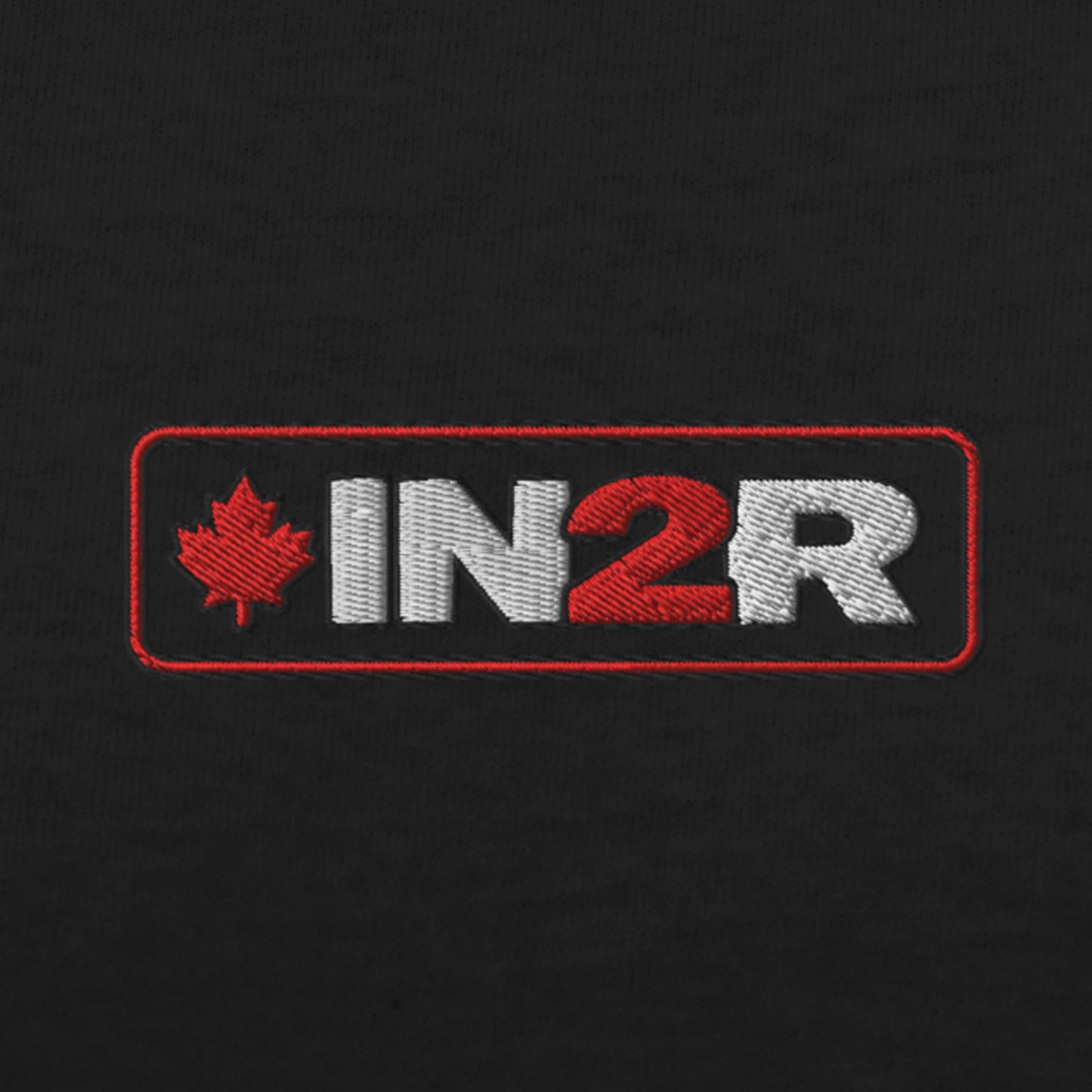 Close-up of an embroidered rectangular logo on black fabric, featuring a red maple leaf and the letters 'IN2R' in white and red.
