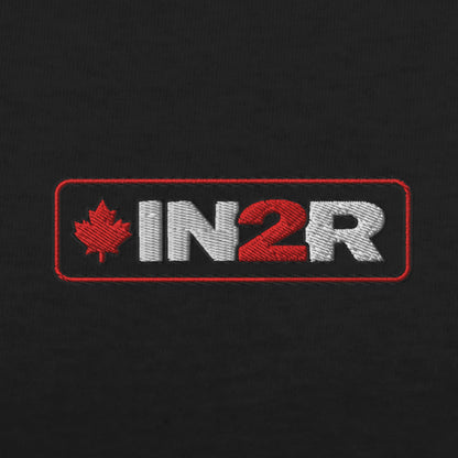 Close-up of an embroidered rectangular logo on black fabric, featuring a red maple leaf and the letters 'IN2R' in white and red.