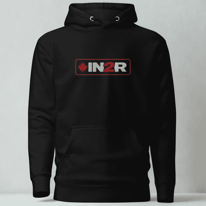 A black pullover hoodie with a front kangaroo pocket and a chest graphic that reads 'IN2R' in white and red with a small red maple leaf, shown against a light gray studio background.