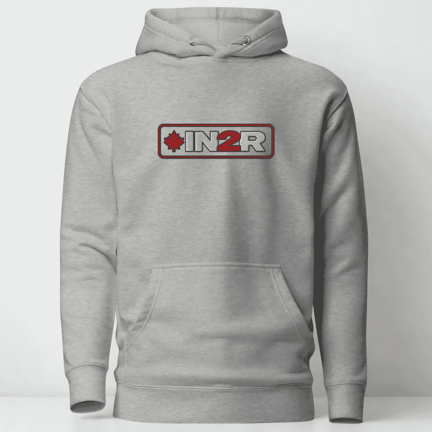 A light gray heather pullover hoodie with a front kangaroo pocket and a chest graphic that reads 'IN2R' with a red maple leaf and red border, shown on a plain light gray background.