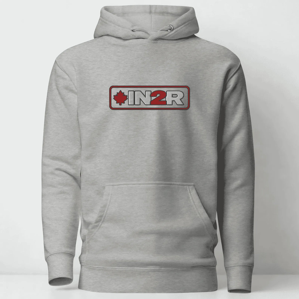 A light gray heather pullover hoodie with a front kangaroo pocket and a chest graphic that reads 'IN2R' with a red maple leaf and red border, shown on a plain light gray background.