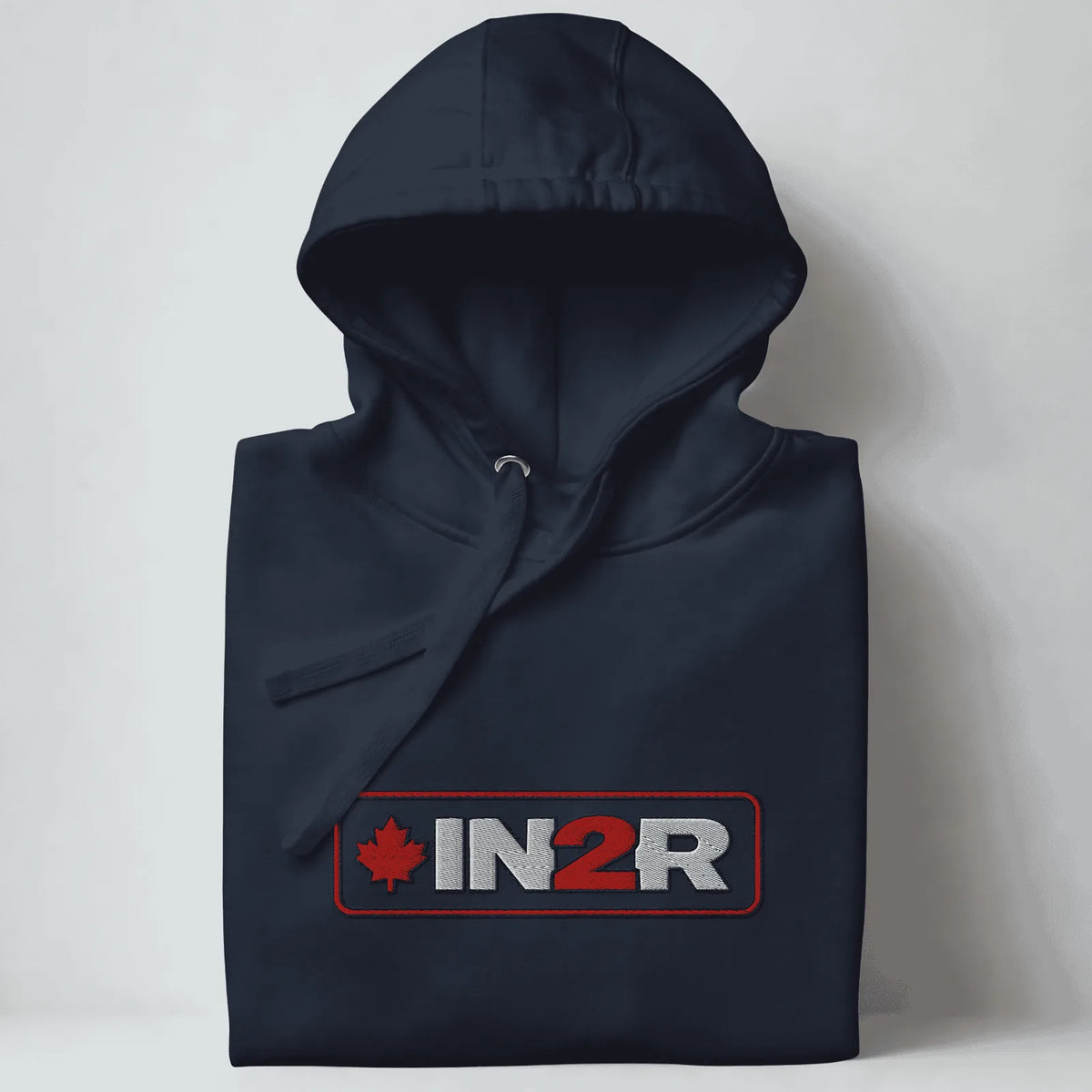 A folded navy blue hooded sweatshirt with a drawstring hood and a front graphic reading 'IN2R' in white and red with a red maple leaf, shown against a light gray background.