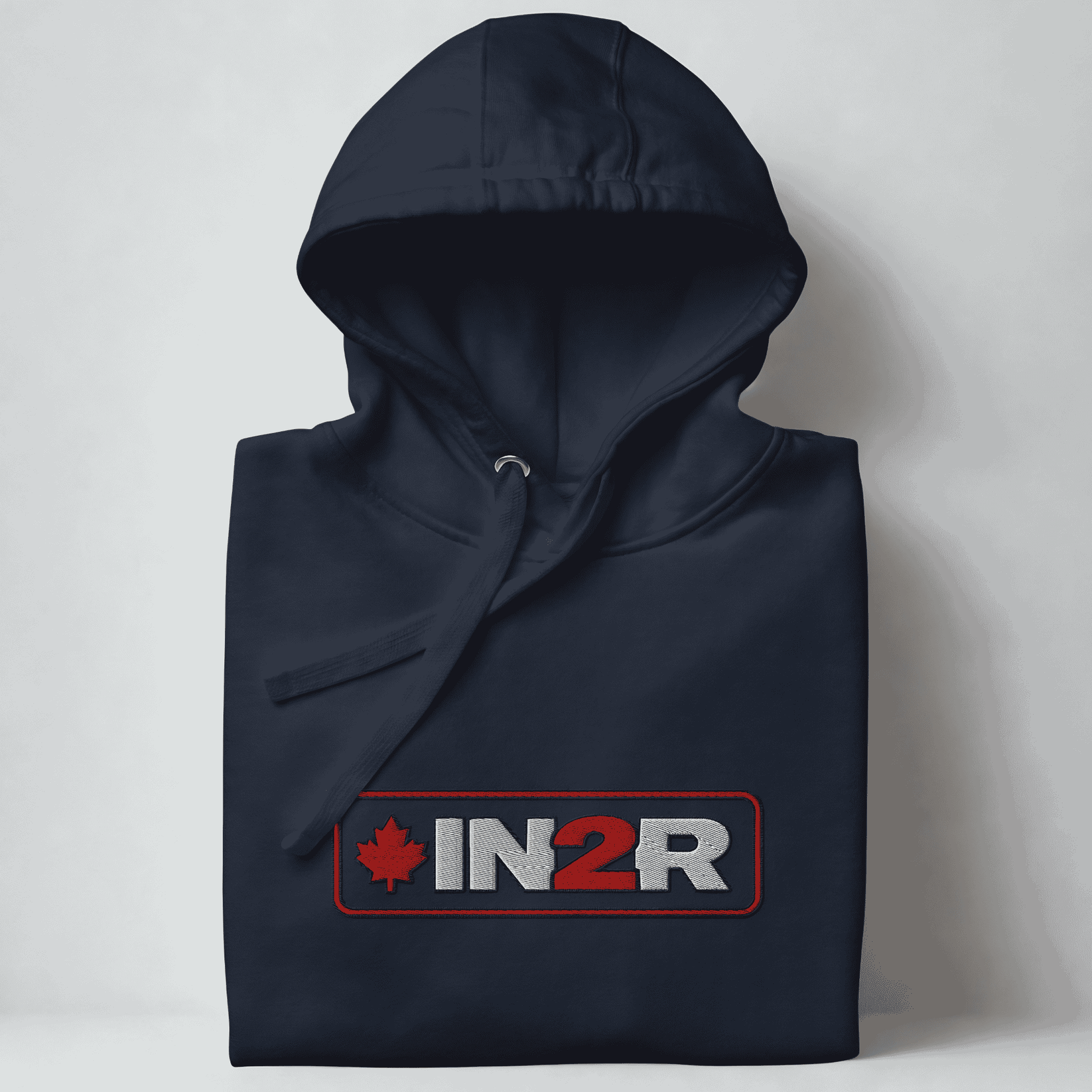 A folded navy hoodie with a drawstring hood, featuring a red and gray 'IN2R' logo with a maple leaf on the chest, set against a light gray background.