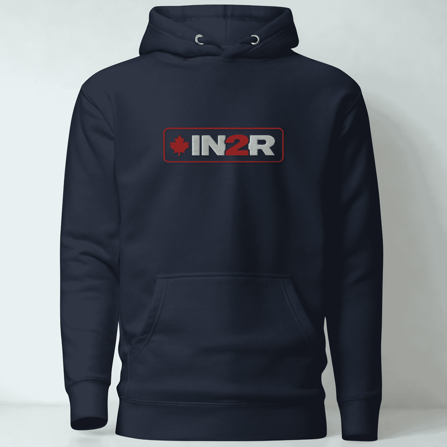 A navy blue pullover hoodie with a front kangaroo pocket and a chest graphic that reads 'IN2R' with a red maple leaf icon, shown against a light gray background.
