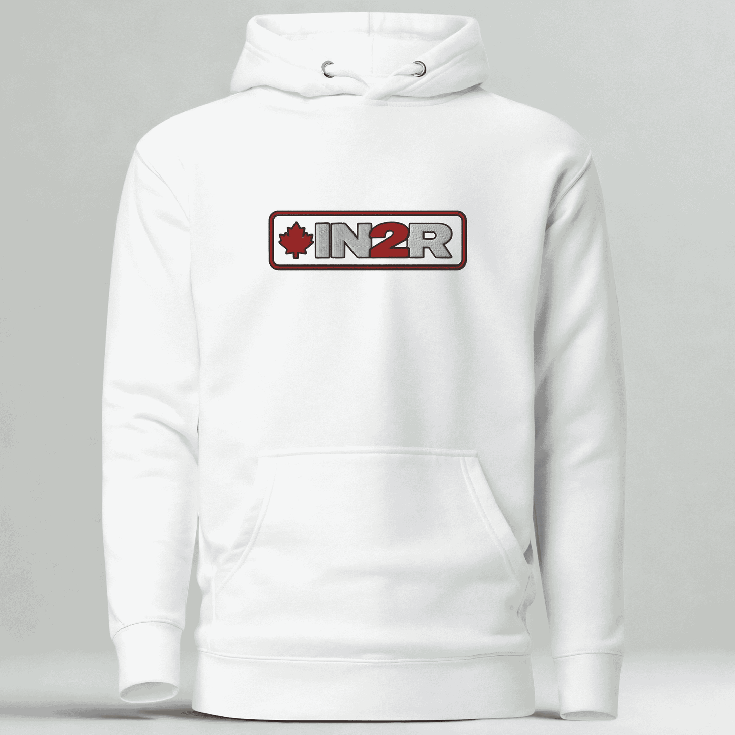 A white pullover hoodie with a front kangaroo pocket and a chest graphic that reads 'IN2R' with a red maple leaf and red border, shown on a light gray studio background.