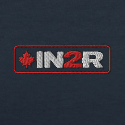 Close-up of an embroidered logo patch on a dark navy fabric background. The patch features a red maple leaf and the letters 'IN2R' in white and red inside a red rectangular border.