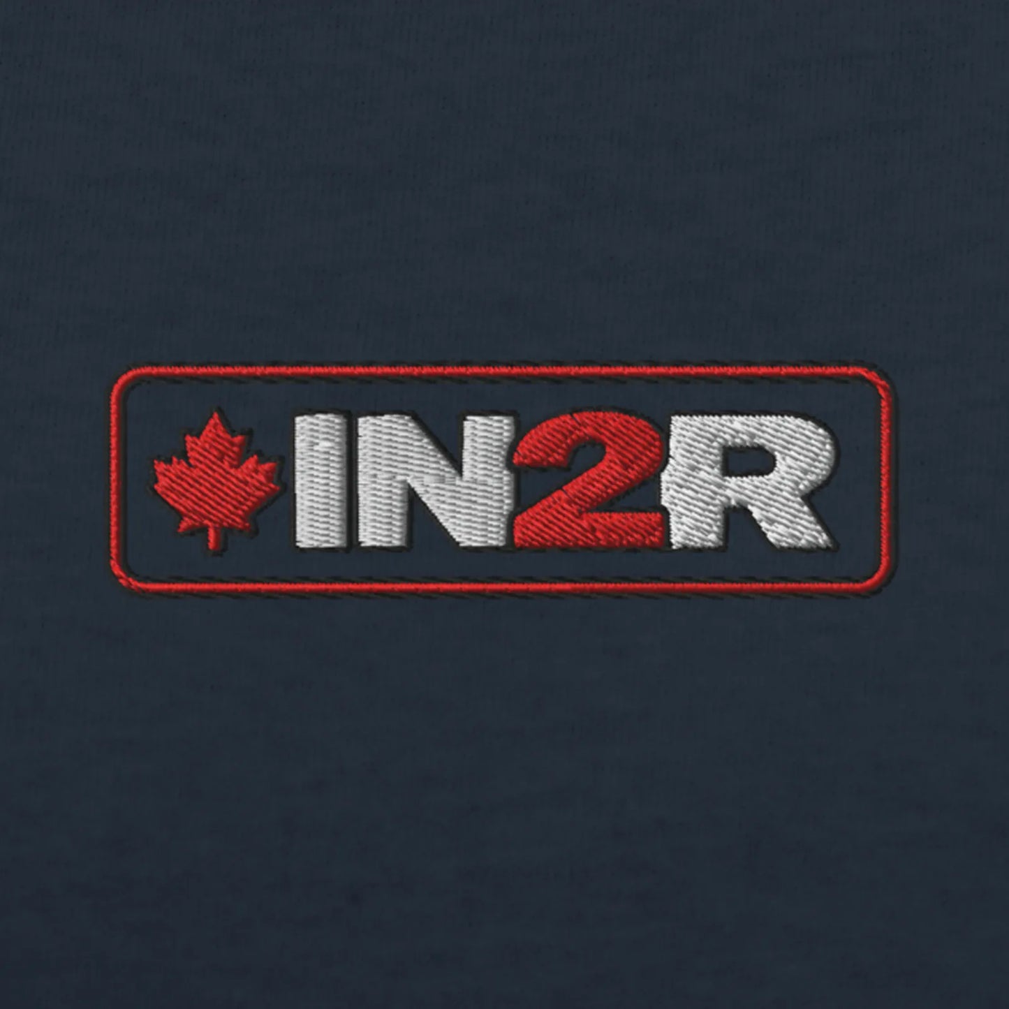 Close-up of an embroidered logo patch on a dark navy fabric background. The patch features a red maple leaf and the letters 'IN2R' in white and red inside a red rectangular border.