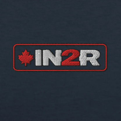 Close-up of an embroidered logo patch on a dark navy fabric background. The patch features a red maple leaf and the letters 'IN2R' in white and red inside a red rectangular border.