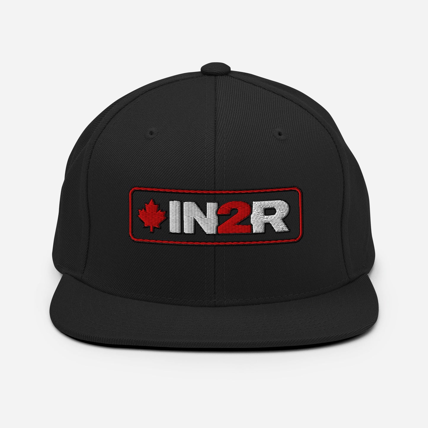 A black snapback cap featuring a rectangular embroidered patch on the front with a red maple leaf, the text 'IN2R' in white and red, and a red border.