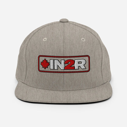 A heather gray snapback cap featuring a rectangular embroidered patch on the front with a red maple leaf, the text 'IN2R' in white and red, and a red border.