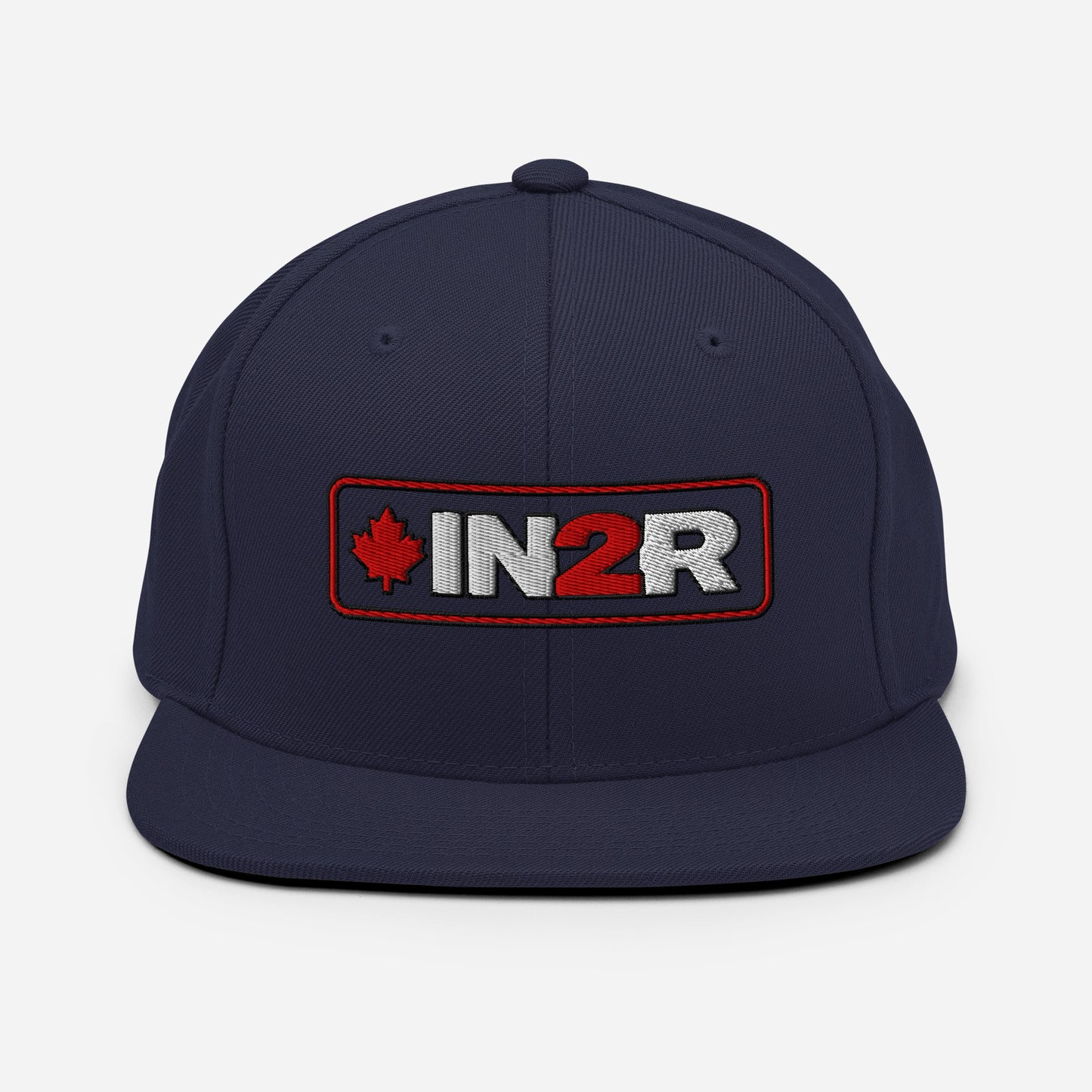 A navy blue flat-brim snapback cap featuring an embroidered front patch with a red maple leaf, the text 'IN2R' in white and red, and a red border.
