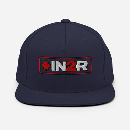 A navy blue flat-brim snapback cap featuring an embroidered front patch with a red maple leaf, the text 'IN2R' in white and red, and a red border.