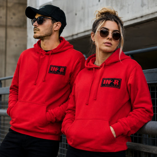 Male and female models wearing the IN2R Classic Red Unisex Hoodie in an urban lifestyle setting, showcasing the premium embroidered IN2R I Need To Ride chest patch.