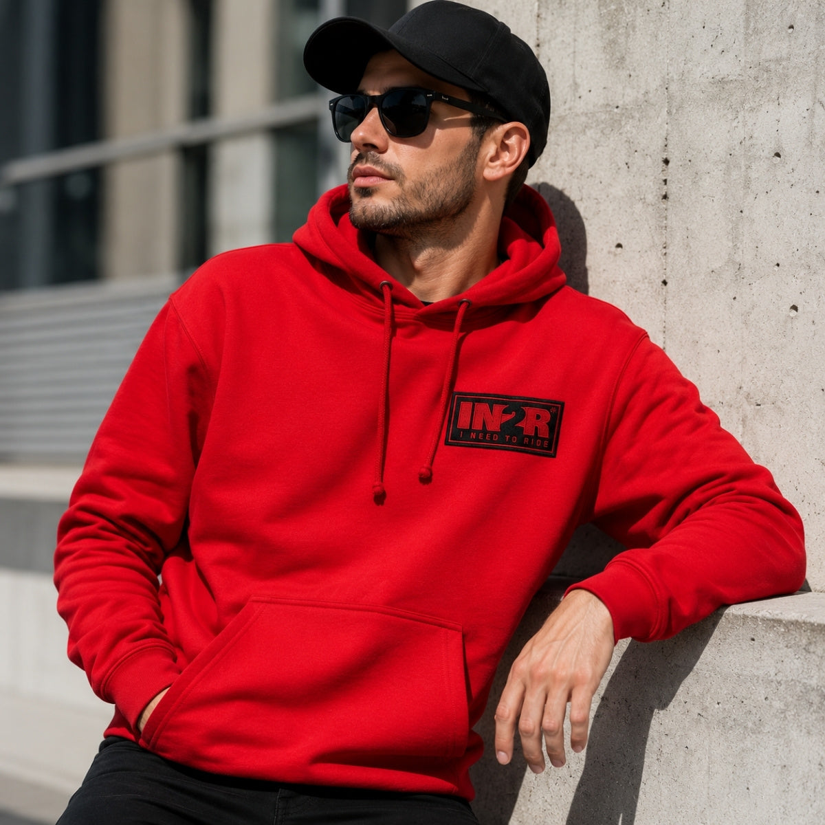 Male model wearing the IN2R Classic Red Unisex Hoodie in an urban lifestyle setting, highlighting the embroidered IN2R I Need To Ride logo patch.