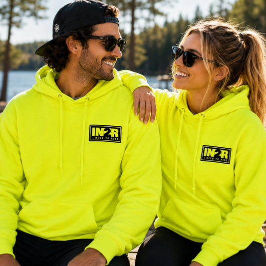 A man and a woman wearing matching neon yellow-green hoodies with a black and yellow 'IN2R' logo on the chest, sitting outdoors near water and trees.