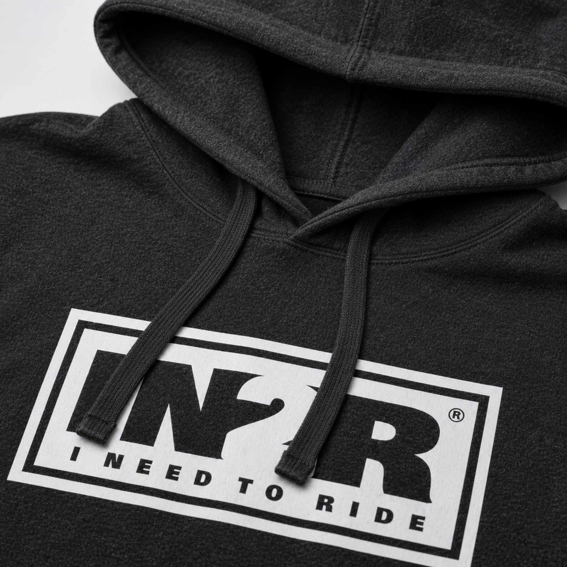 Close-up of a dark charcoal gray hoodie featuring a bold white rectangular graphic on the chest with the letters 'IN2R' and the text 'I NEED TO RIDE'.