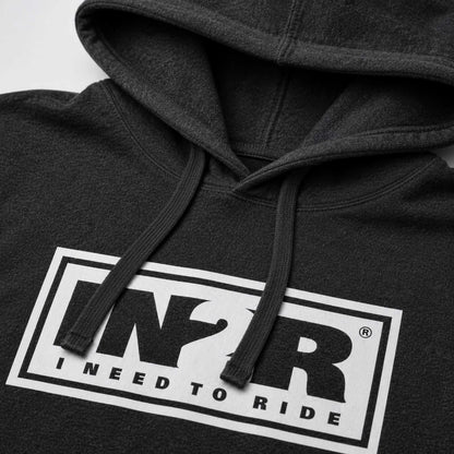 Close-up of a dark charcoal gray hoodie featuring a bold white rectangular graphic on the chest with the letters 'IN2R' and the text 'I NEED TO RIDE'.