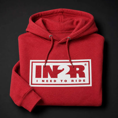 A folded red hoodie with a white rectangular chest graphic reading 'IN2R I NEED TO RIDE' in red and white, shown on a dark background.