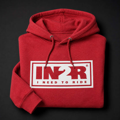 A folded red hoodie with a white rectangular chest graphic reading 'IN2R I NEED TO RIDE' in red and white, shown on a dark background.