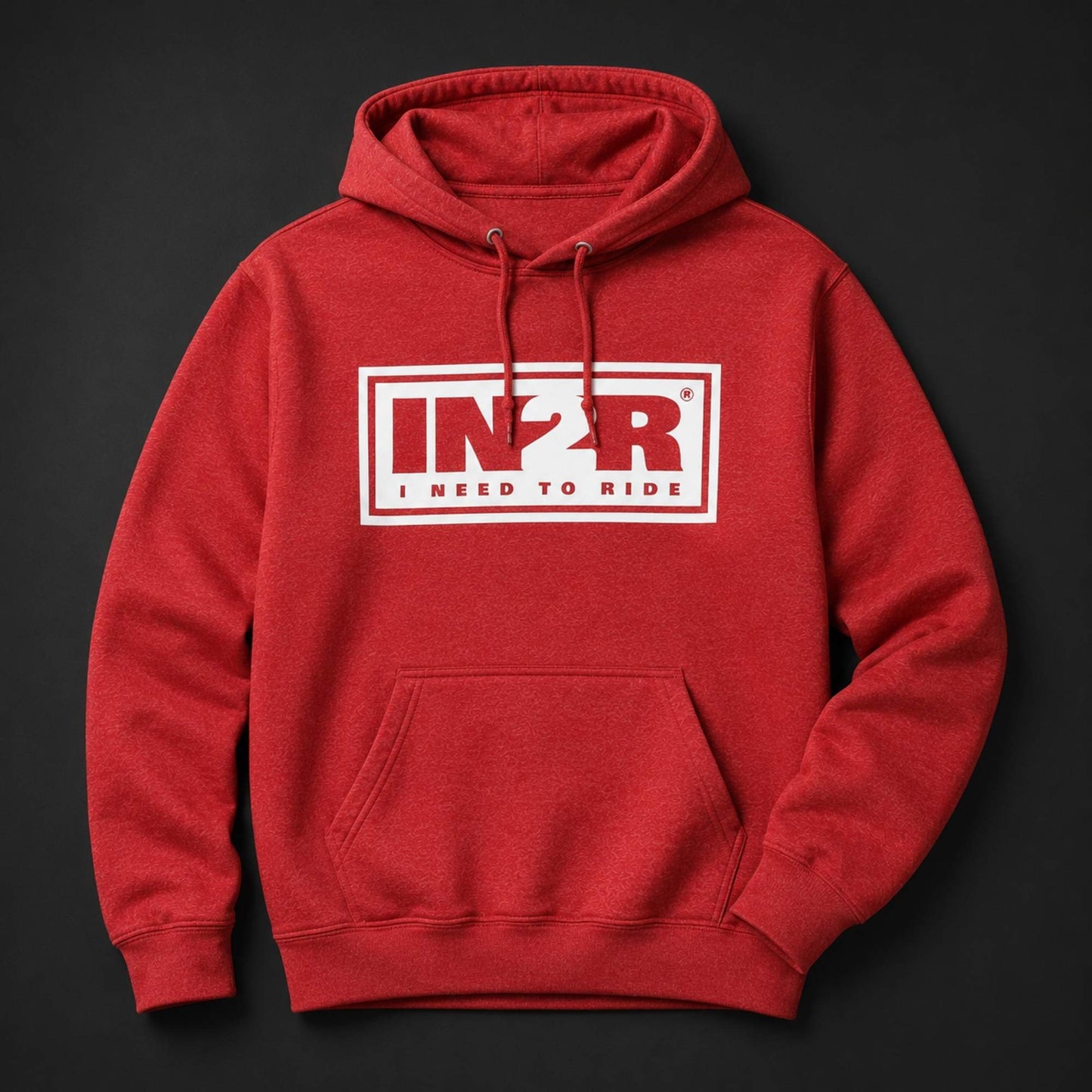A red pullover hoodie with a white rectangular chest graphic reading 'IN2R I NEED TO RIDE' in red and white, shown on a dark charcoal background.