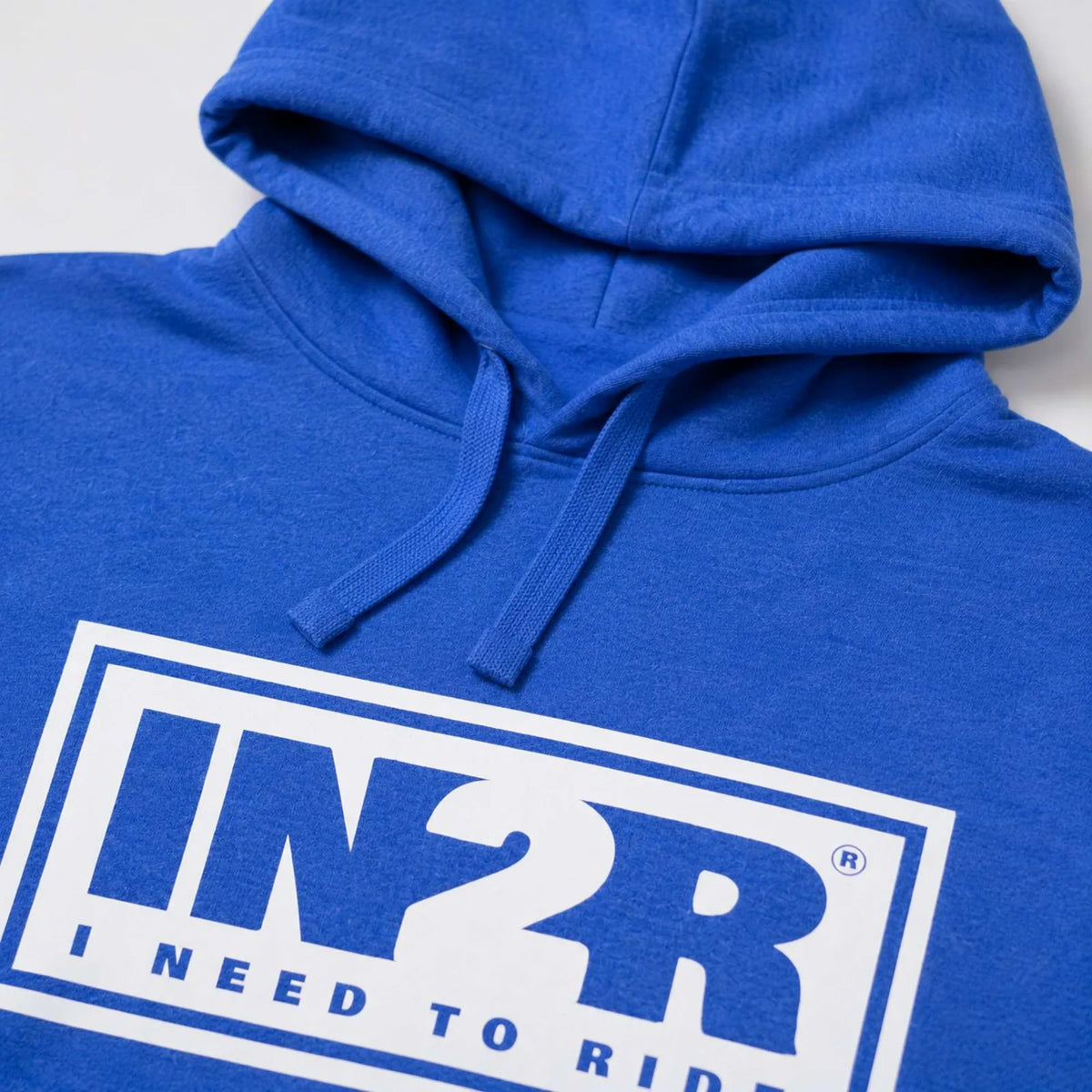 A close-up of a royal blue hoodie featuring a white graphic box on the chest with the text 'IN2R' and 'I NEED TO RIDE' in blue.
