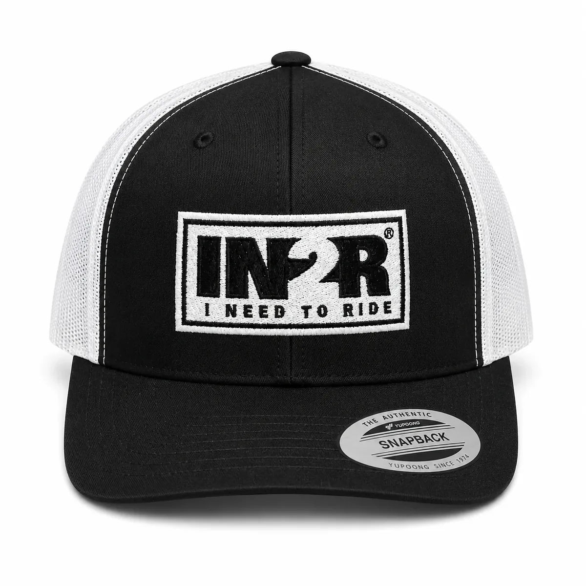 A black and white trucker hat with a black front panel, white mesh back, and a white rectangular patch on the front that reads 'IN2R RIDE I NEED TO RIDE'. A silver 'Snapback' sticker is visible on the brim.