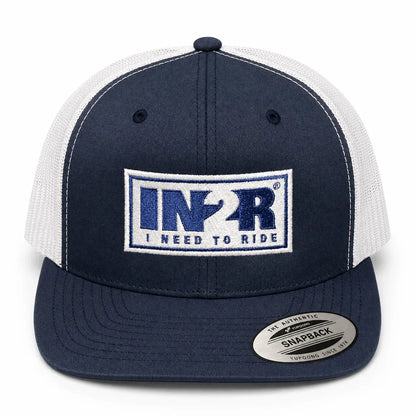A navy blue and white trucker hat with a front patch reading 'IN2R I NEED TO RIDE' and a Snapback sticker on the brim, shown on a white background.