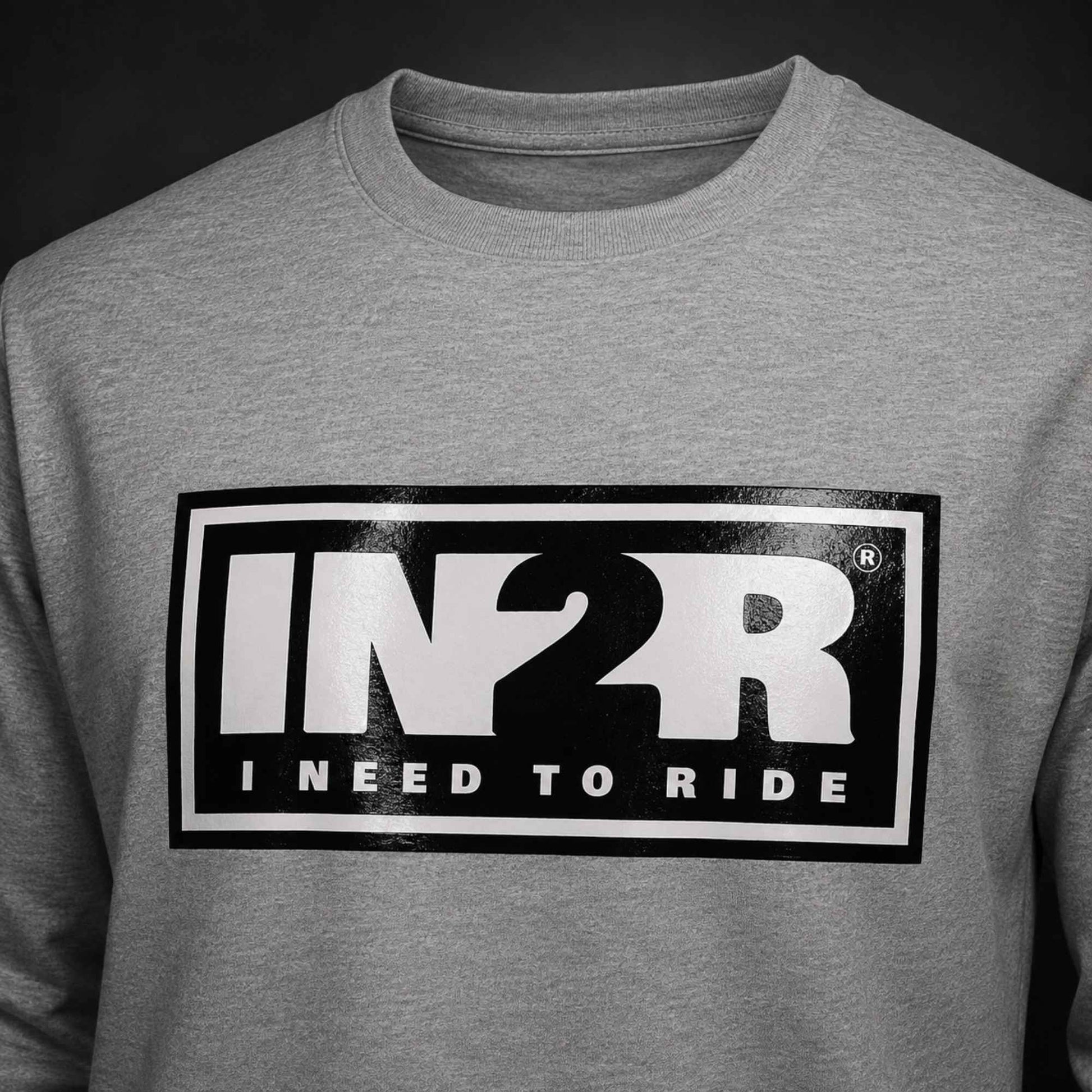 A close-up of a heather gray crewneck sweatshirt featuring a large black and white graphic on the chest with the text 'IN2R' and 'INEED TO RIDE'.