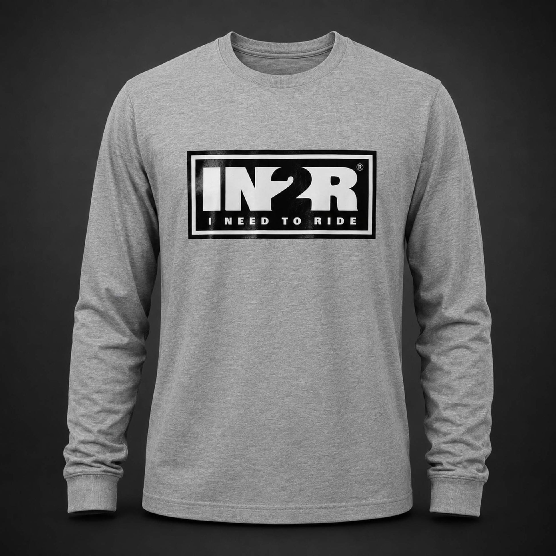 A heather gray long-sleeve t-shirt with a black and white 'IN2R I NEED TO RIDE' graphic on the chest, displayed on a dark gray background.